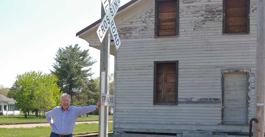 Harold Thorpe leans against the train crossing sign